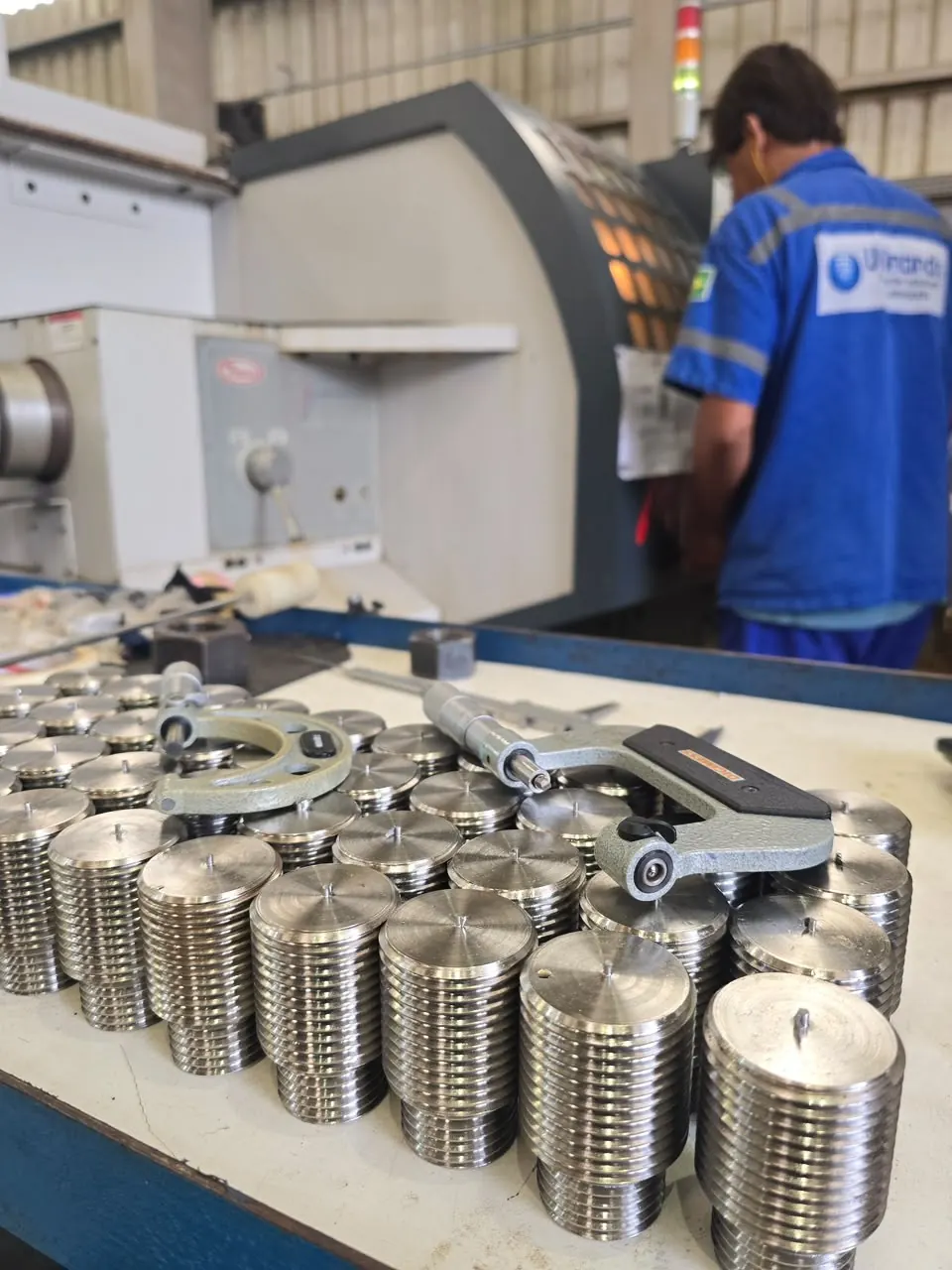 Profissional da Usinando no torno CNC, com peças roscadas e micrômetros na bancada